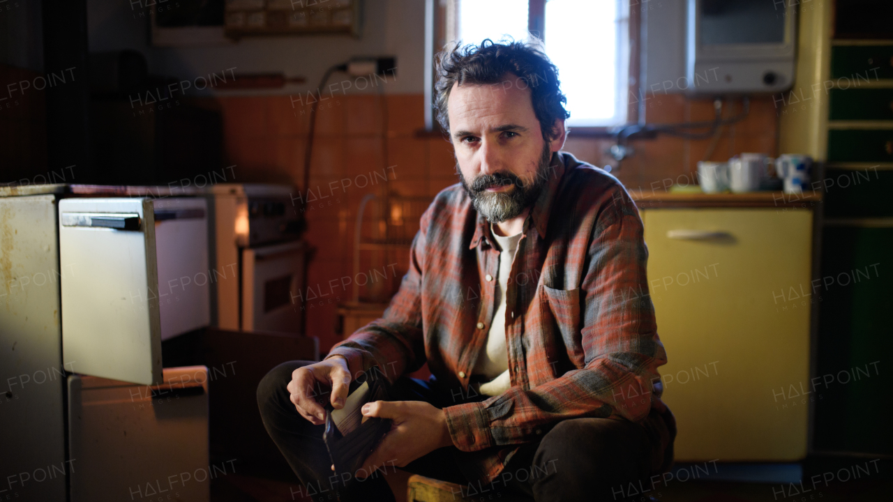 Portrait of poor mature man with empty wallet looking at camera indoors at home, poverty concept.