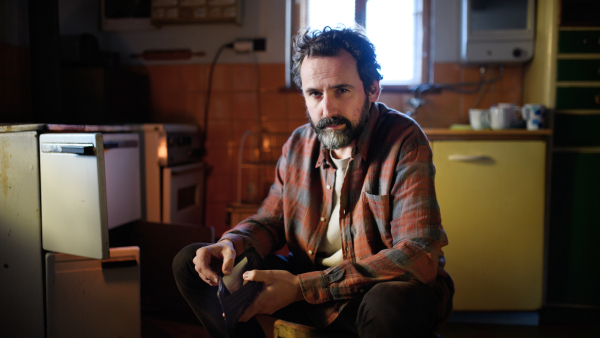 Portrait of poor mature man with empty wallet looking at camera indoors at home, poverty concept.