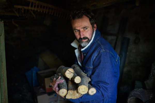 Poor mature man gathering firewood in shed at home, poverty concept.