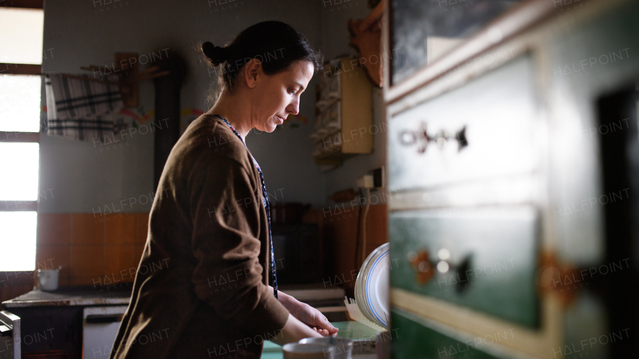 Portrait of poor mature woman washing dishes indoors at home, poverty concept.