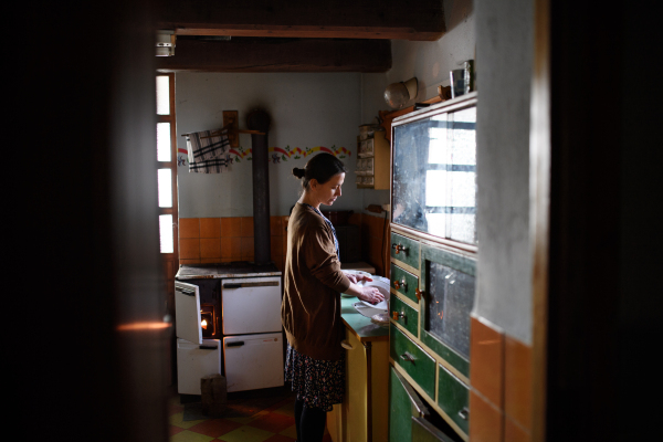 A portrait of poor mature woman indoors at home washing dishes, poverty concept.