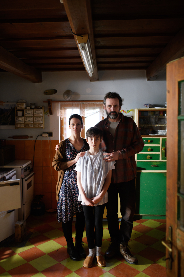 Portrait of poor mature couple with small daughter indoors in kitchen at home, poverty concept.