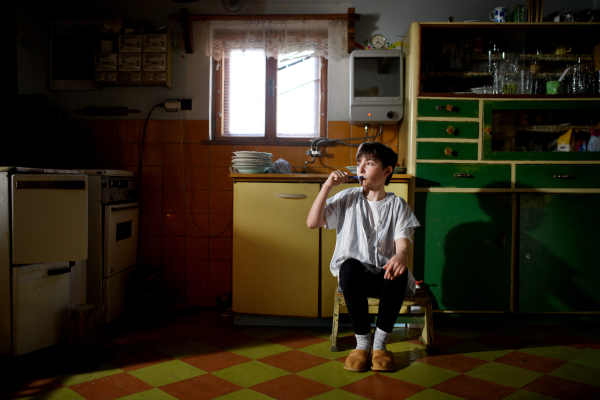 Portrait of small girl brushing teeth in kitchen indoors at home, poverty concept.