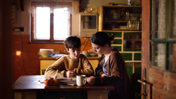 A poor mature mother and small daughter learning indoors at home, poverty concept.