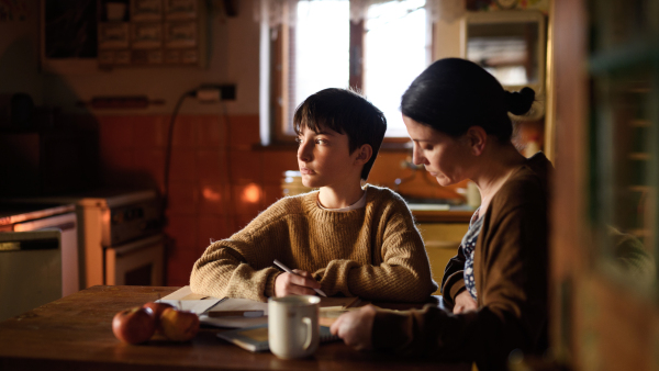 A poor mature mother and small daughter learning indoors at home, poverty concept.