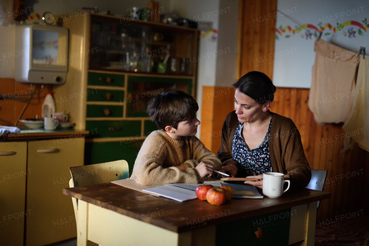 A poor mature mother and small daughter learning indoors at home, poverty concept.