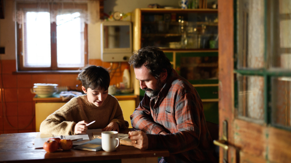 A poor mature father and small daughter learning indoors at home, poverty concept.