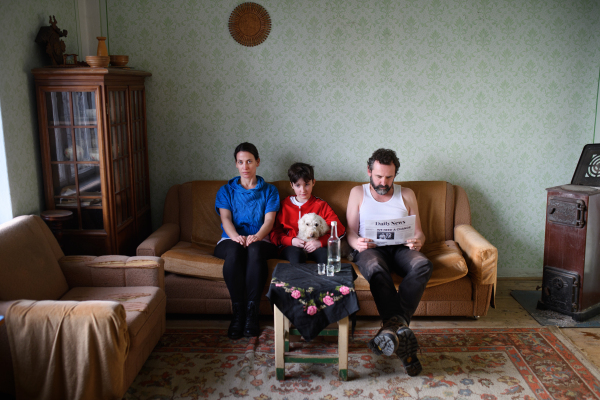 Portrait of poor mature couple with small daughter indoors on sofa at home, poverty concept.