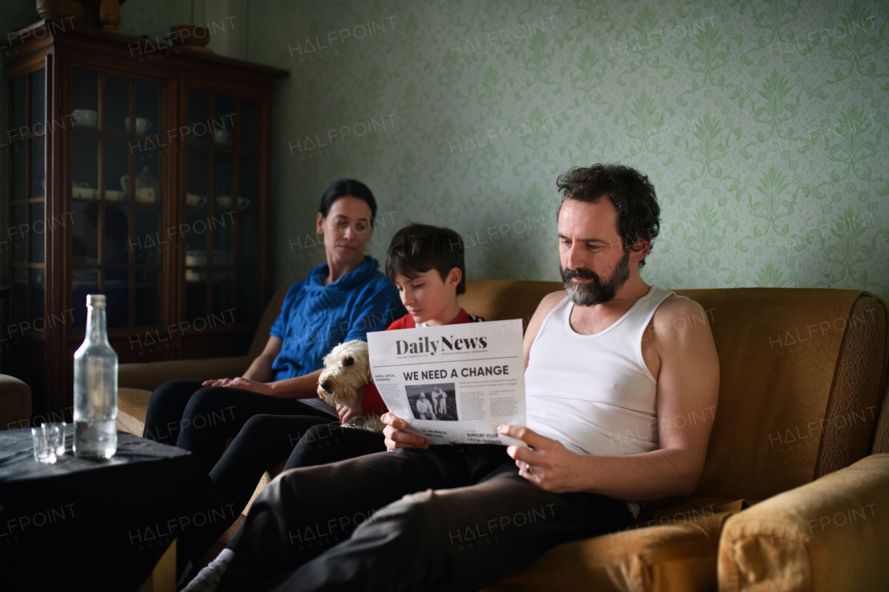 Portrait of poor mature couple with small daughter and dog indoors on sofa at home, poverty concept.