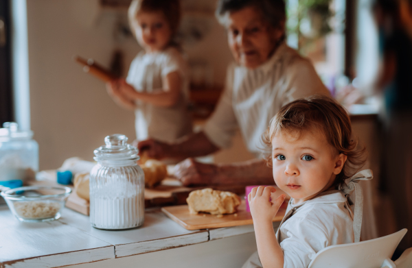 Happy senior great grandmother with small toddler children making cakes at home.