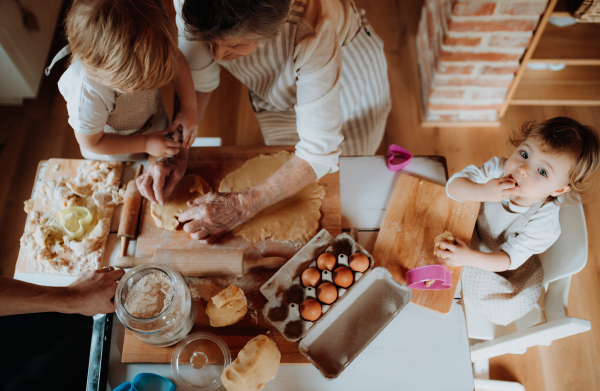 A top view of senior great grandmother with small toddler children making cakes at home.