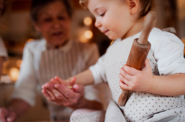 A senior great grandmother with small toddler grandchild making cakes at home.