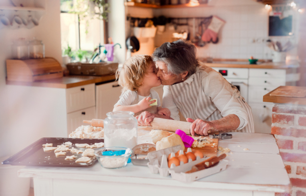 Happy senior great grandmother with small toddler boy making cakes at home, kissing.