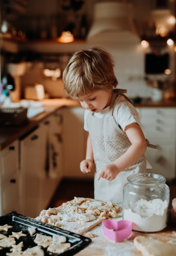 A happy small toddler boy making cakes in a kitchen at home.