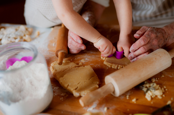 A midsection of senior great grandmother with small toddler boy making cakes at home.