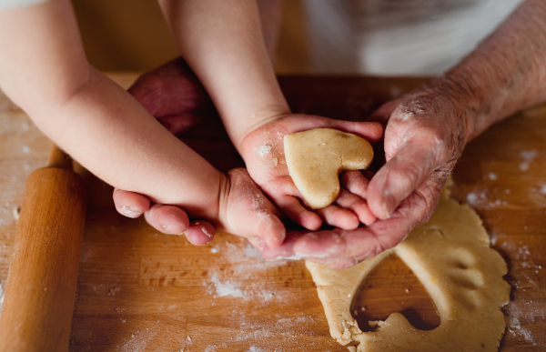 A midsection of senior great grandmother with small toddler boy making cakes at home. A close-up.