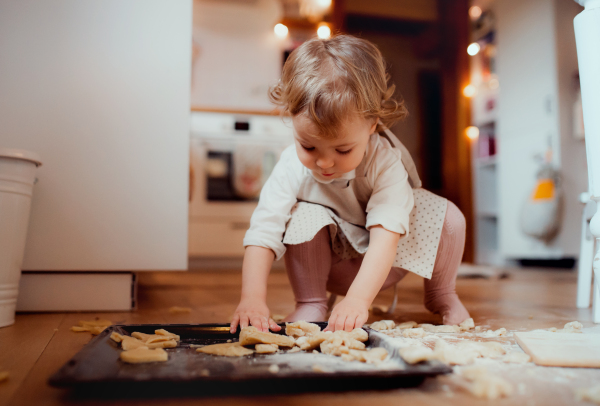 A content small toddler girl making cakes on the floor in the kitchen at home.