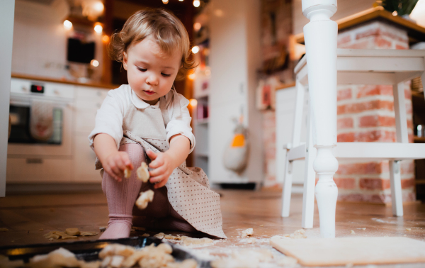 A content small toddler girl making cakes on the floor in the kitchen at home.