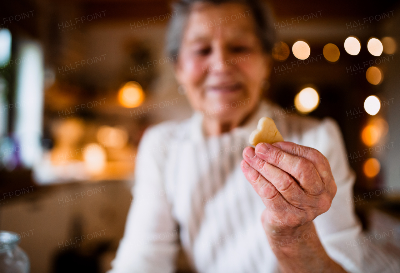 A close-up of happy elderly woman making cakes in a kitchen at home, holding a biscuit.