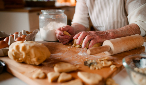 A midsection of old woman making cakes in a kitchen at home.