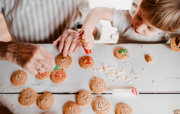 A midsection of senior grandmother with small toddler boy making and decorating cakes at home. A top view.