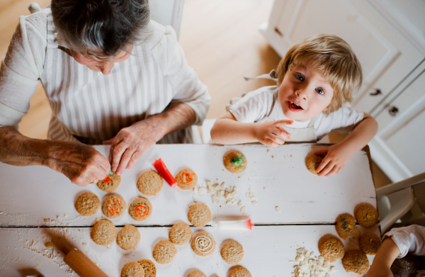 A top view of senior grandmother with small toddler boy making and decorating cakes at home.