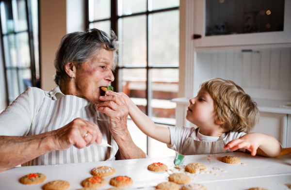 Happy senior great grandmother with small toddler boy making and eating cakes at home.