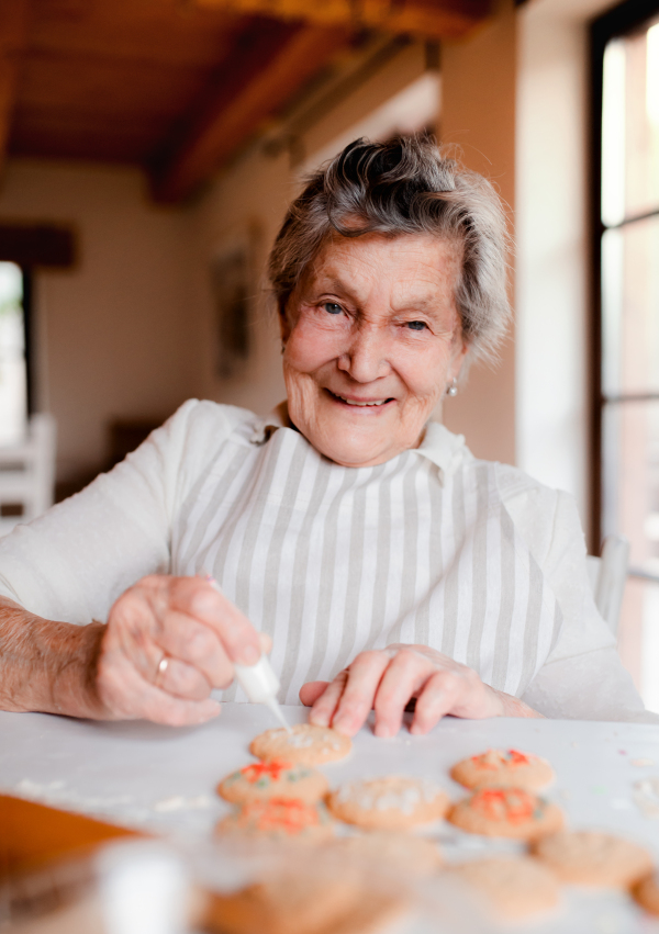 An elderly woman making and decorating cakes in a kitchen at home.