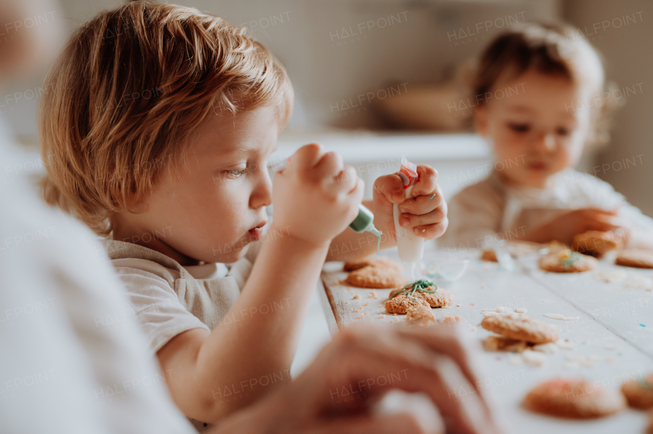 Two happy small toddler children sitting at the table, decorating and eating cakes at home.