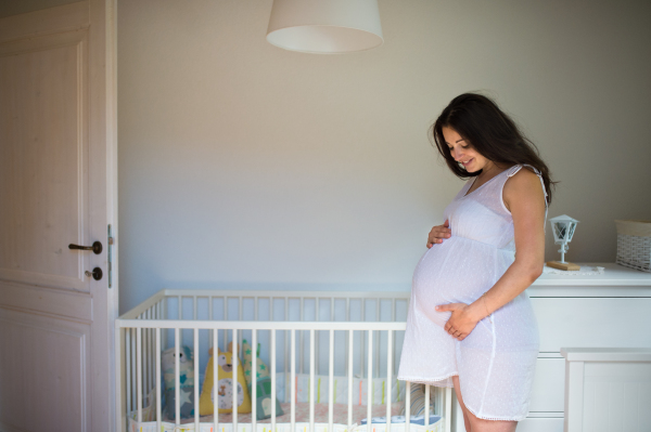 Portrait of happy pregnant woman indoors at home, touching her belly. Copy space.