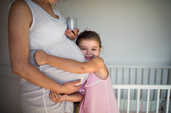 Portrait of unrecognizable pregnant woman with small daughter indoors at home, hugging.