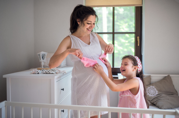 Portrait of pregnant woman with small daughter indoors at home, having fun.