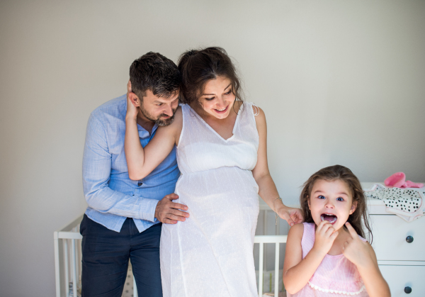 Front view portrait of pregnant woman with husband and small daughter indoors at home.