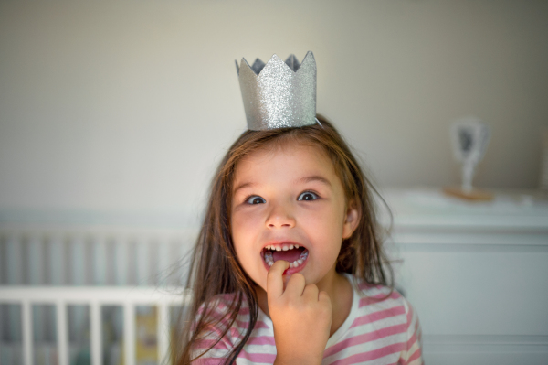 Portrait of happy small girl with princess crown on head indoors, looking at camera.