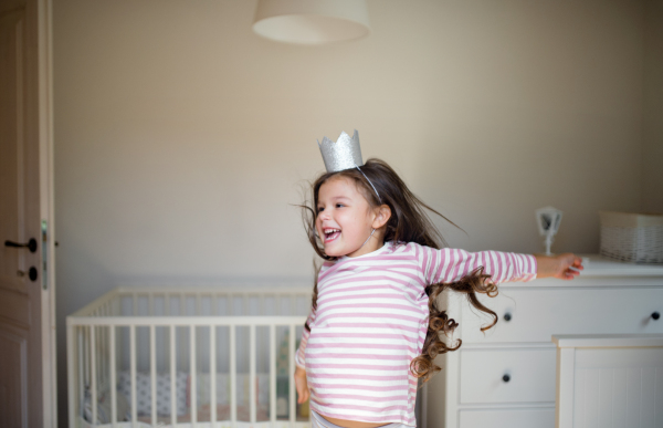 Portrait of happy small girl with princess crown on head indoors, having fun.