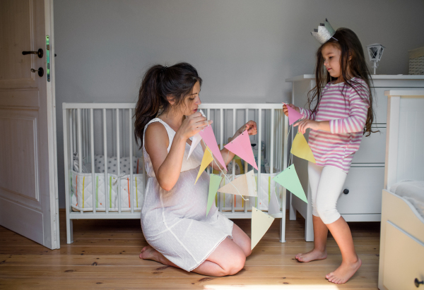 Portrait of happy pregnant woman with small daughter indoors at home, decorating bedroom.