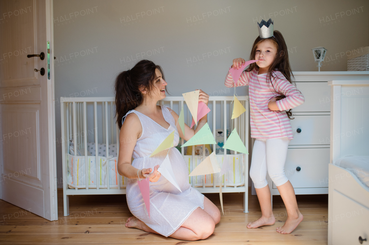 Portrait of happy pregnant woman with small daughter indoors at home, playing.