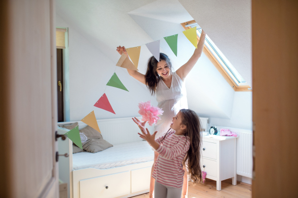 Portrait of happy pregnant woman with small daughter indoors at home, decorating bedroom.