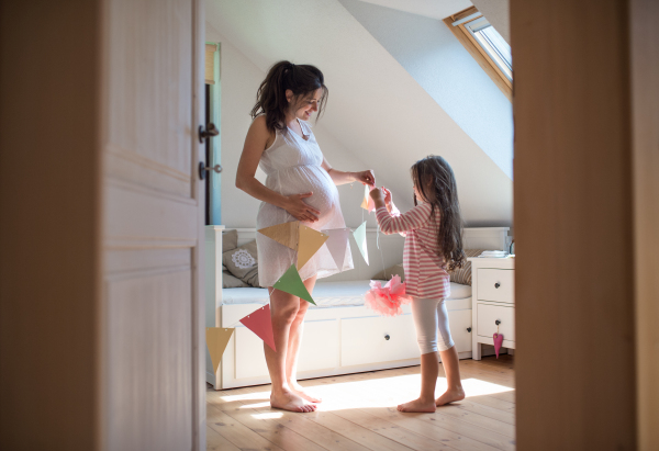 Portrait of happy pregnant woman with small daughter indoors at home, decorating bedroom.