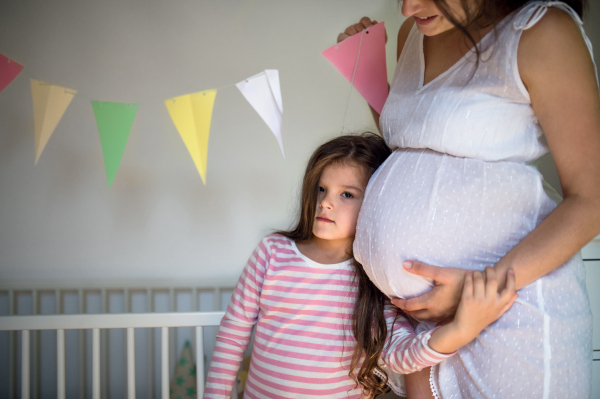 Portrait of unrecognizable happy pregnant woman with small daughter indoors at home.