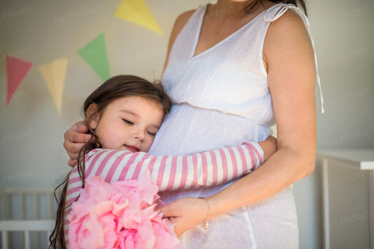 Unrecognizable pregnant woman with small daughter indoors at home, hugging.