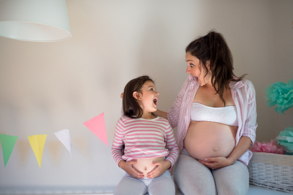 Portrait of pregnant woman with small daughter indoors at home, having fun.