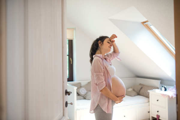 Side view portrait of tired pregnant woman indoors at home, holding head.