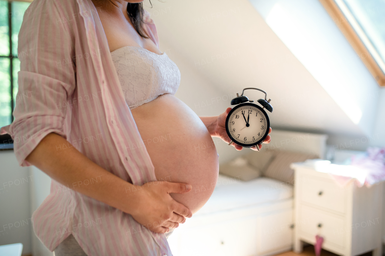 Unrecognizable pregnant woman with clock set to five to twelve indoors at home, due date concept.