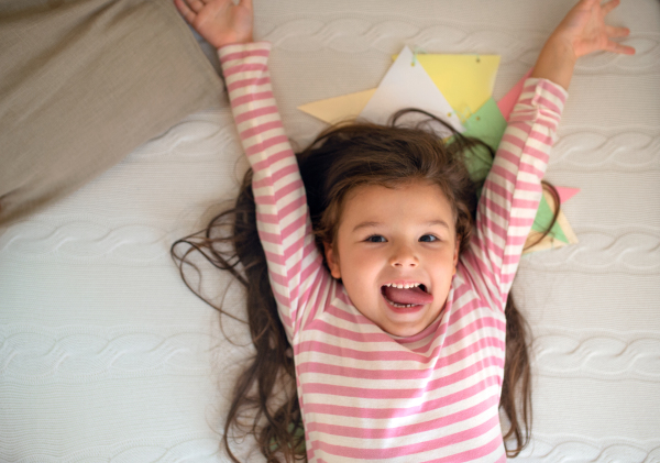 Top view portrait of small girl lying on bed indoors, looking at camera.