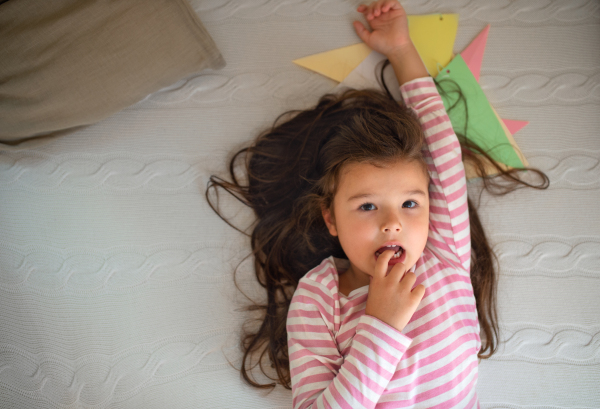 Top view portrait of small girl lying on bed indoors, looking at camera.