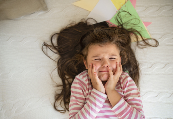 Top view portrait of unhappy small girl lying on bed indoors, crying.