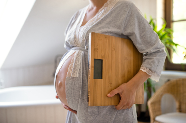 Midsection of unrecognizable pregnant woman indoors at home, carrying scales.