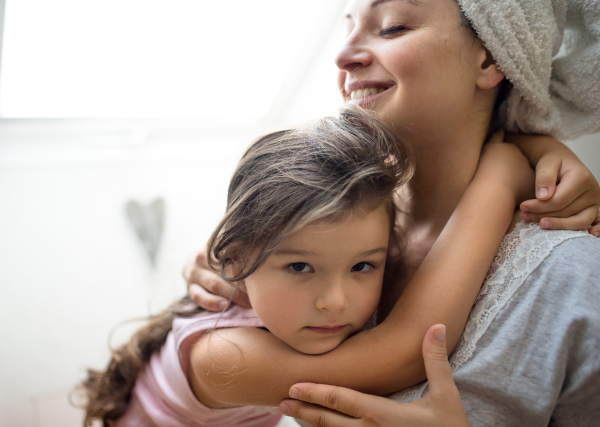 Portrait of mother and small daughter indoors at home, hugging.