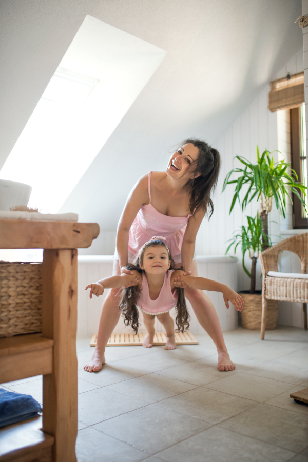 Portrait of happy pregnant woman with small daughter indoors in bathroom at home, having fun.